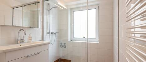 Un baño moderno con cabina de ducha de vidrio, lavamanos empotrado y ventana que proporciona luz natural.