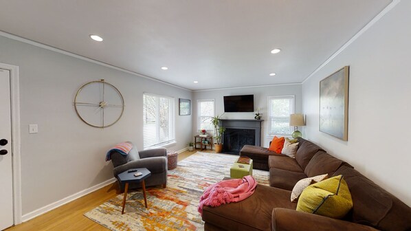 A living room with a fireplace, a sofa, a coffee table, and a TV mounted on the wall.