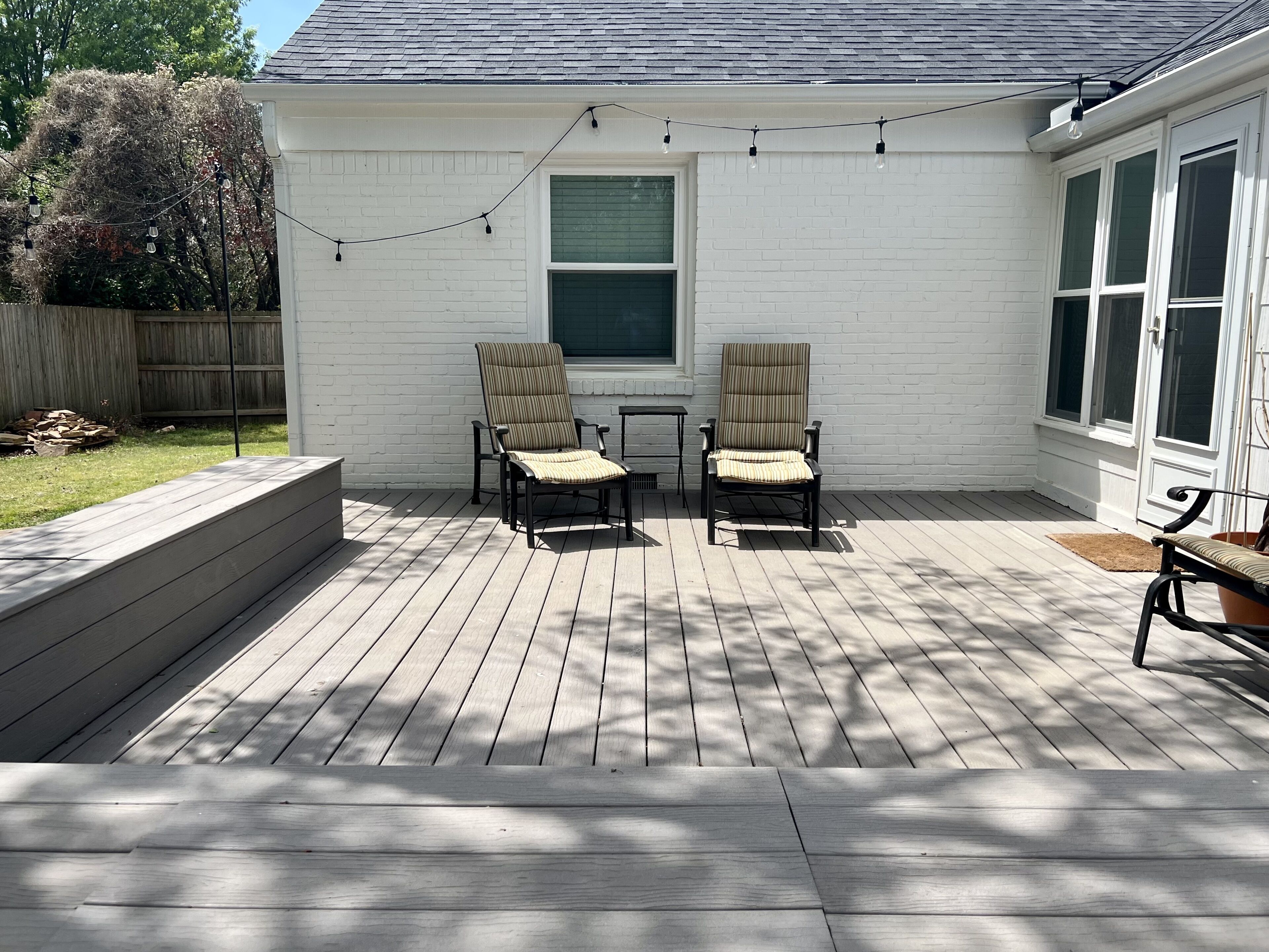 A covered patio with two chairs and a small table, a white exterior wall, and a window.