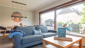 Una sala de estar moderna con un sofá gris, una mesa de centro de madera y un ventanal con vistas a una zona residencial.