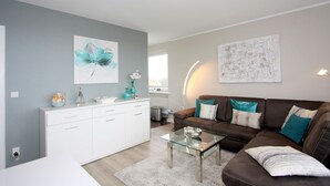 Un salon moderne avec un canapé en cuir marron, une table basse en verre et un meuble blanc. Un tableau est accroché au mur et une lampe se trouve sur la table d’appoint.