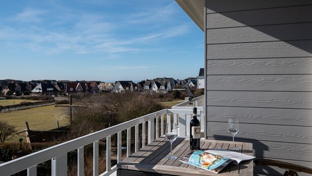 Une terrasse en bois avec une balustrade blanche donnant sur un quartier résidentiel.
