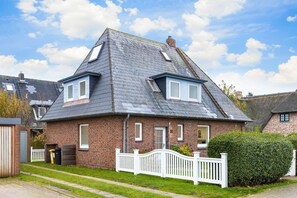 Una casa a due piani con un tetto ripido, rivestimento in mattoni e una recinzione in legno bianco.