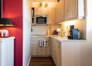A compact kitchen with wooden cabinets, a microwave, a coffee maker, and a small sink.