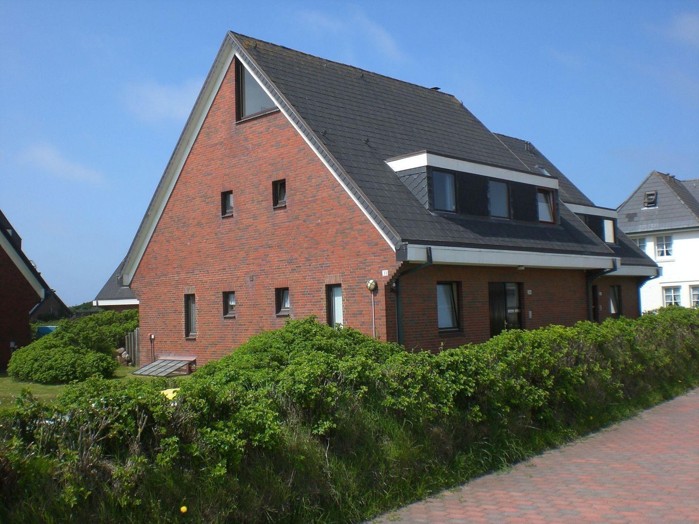 Een huis met twee verdiepingen, een schuin dak, een bakstenen gevel en een klein voortrekje.