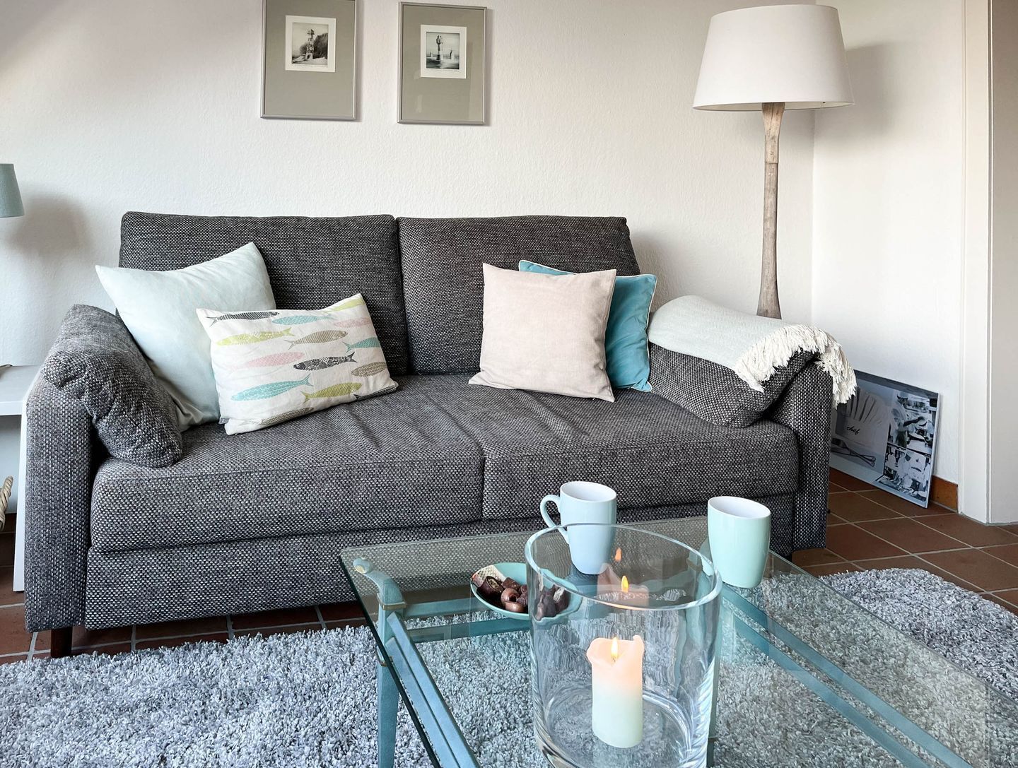 A grey sofa with patterned cushions, a glass coffee table with a candle, and a lamp.