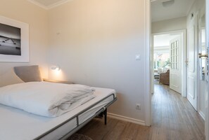 Un dormitorio con cama, mesita de noche, lámpara de pared y puerta que da a una sala de estar.