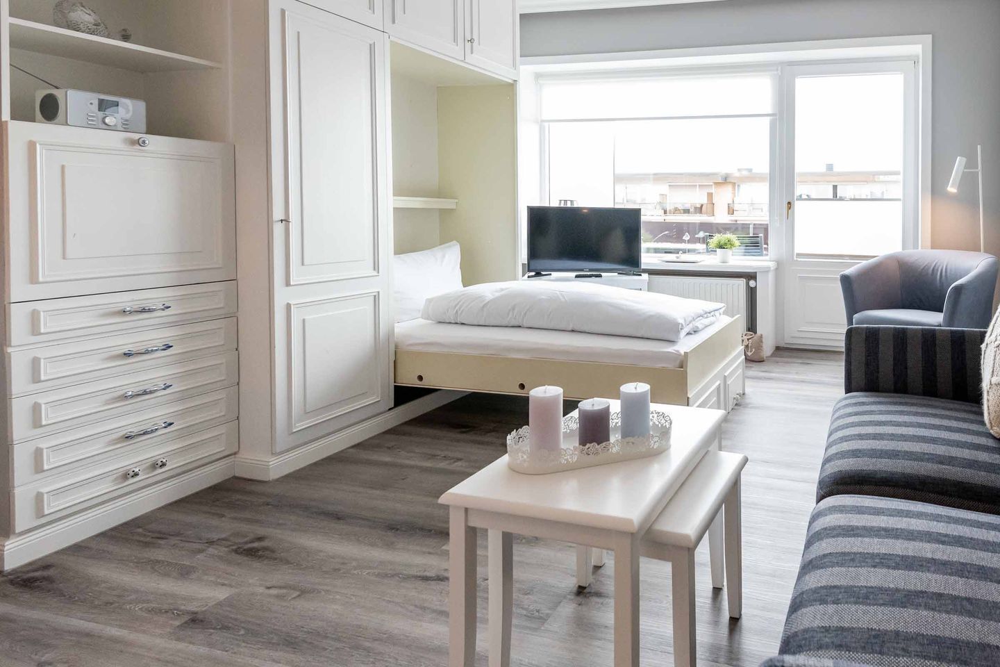 A bedroom with a bed, a TV, a desk with candles, a sofa, and a wardrobe.