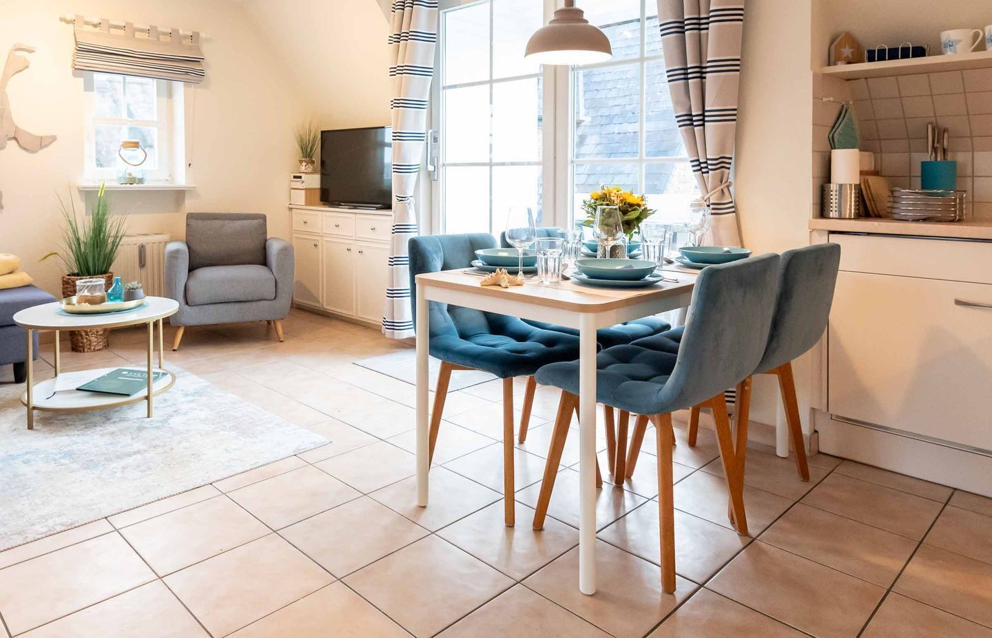 Een moderne keuken met een eettafel voor vier personen, een grijze bank en een televisie op de achtergrond.