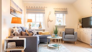 A modern living room with a grey sofa, a small round table, a grey armchair, and a television on a cabinet. - SyltStern Haus Hasenkuhle - Bright 3-room apartment with approx. 55m², for up to 4 persons. (Wenningstedt-Braderup (Sylt))