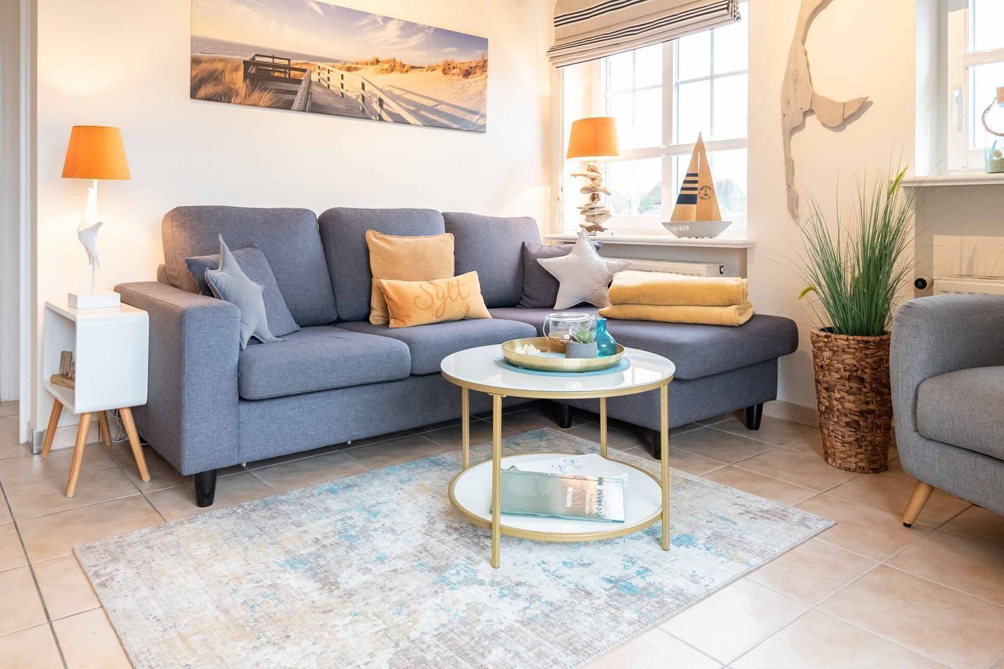 Un salon moderne avec un canapé gris, une petite table basse ronde et une grande fenêtre donnant sur la plage.