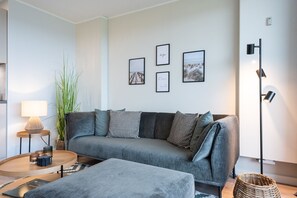 A modern living room with a grey sofa, a round coffee table, a floor lamp, and framed pictures on the wall. - Lichtblick im Haus Cäcilia - Modern 2-room apartment with beautiful balcony (Wenningstedt-Braderup (Sylt))