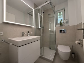 Ein modernes Badezimmer mit Duschabtrennung aus Glas, einem weißen Waschbecken und einer Toilette.