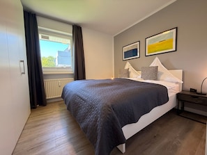 Una camera da letto con un letto, una finestra con tende, un termosifone e due quadri appesi al muro.