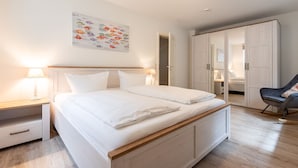 A bedroom with a bed, bedside tables, a chair, a wardrobe, and a wall art piece. - LH Heidegrund, App.2 - 3-room apartment in direct beach location with approx. 75m² (Wenningstedt-Braderup (Sylt))