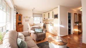 A living room with a sofa and armchairs, a dining area with a table, and a kitchen with cabinets and appliances. - LH Heidegrund, App.2 - 3-room apartment in direct beach location with approx. 75m² (Wenningstedt-Braderup (Sylt))