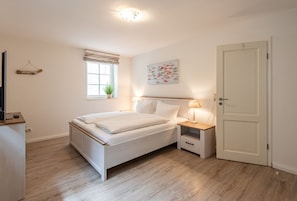A bedroom with a bed, bedside tables, a window with curtains, a wall-mounted artwork, and a door.