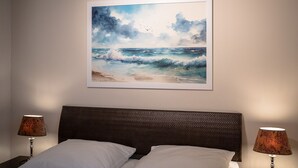 Un dormitorio con una cama, dos lámparas de noche y un cuadro enmarcado con una playa.