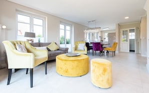 A spacious living room with a sofa, armchairs, and ottomans. There is a dining area with chairs and a table. - Hüs Maxi - Luxury house in a popular residential area on approx. 170 m² for up to 7 people. (Wenningstedt-Braderup (Sylt))
