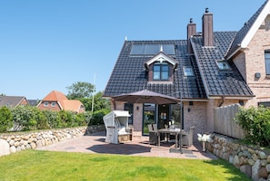 A house with a sloped roof, a patio with outdoor furniture, and a stone wall. - Hüs Maxi - Luxury house in a popular residential area on approx. 170 m² for up to 7 people. (Wenningstedt-Braderup (Sylt))