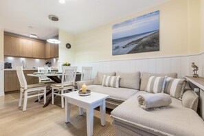 Ein gemütliches Wohnzimmer mit einer Couch, Sesseln, einem Esstisch und einer Küchenzeile.