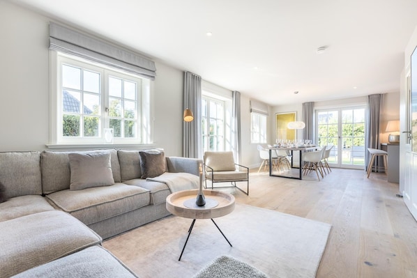 A modern living room with a sofa, a coffee table, and a dining area with chairs and a table.