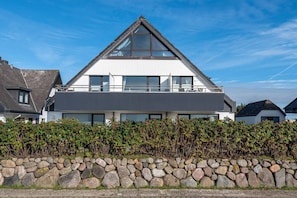 Ett modernt hus i två våningar med en stenvägg på framsidan, stora fönster och ett sluttande tak.