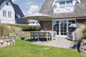 Ein Haus mit Terrasse, einem Tisch mit Stühlen, einem großen Sonnenschirm und einer Steinmauer.
