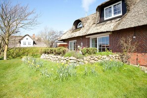 Et traditionelt hus med stråtækt tag, en stenvæg og en have med påskeliljer.