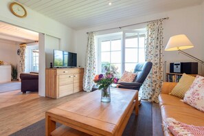 En stue med et træsofabord, en sofa, et fjernsyn på et træskab og en lænestol.
