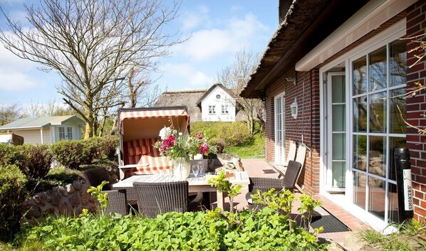 En terrasse med et bord, stole, en blomstervase og en murstensvæg med et vindue.
