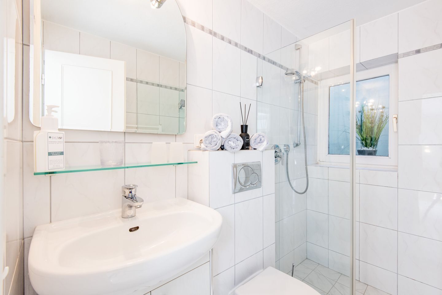A modern bathroom with a glass shower enclosure, a white sink, and a large mirror.