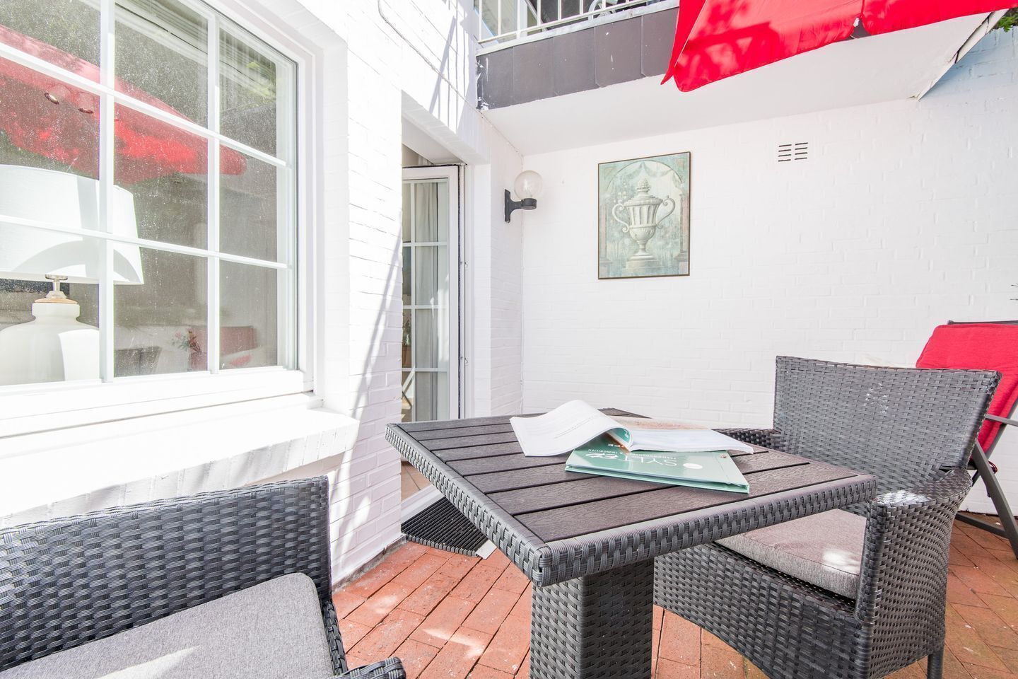 Eine Terrasse mit Tisch und Stühlen, einem roten Sonnenschirm und einem gerahmten Bild an der Wand.