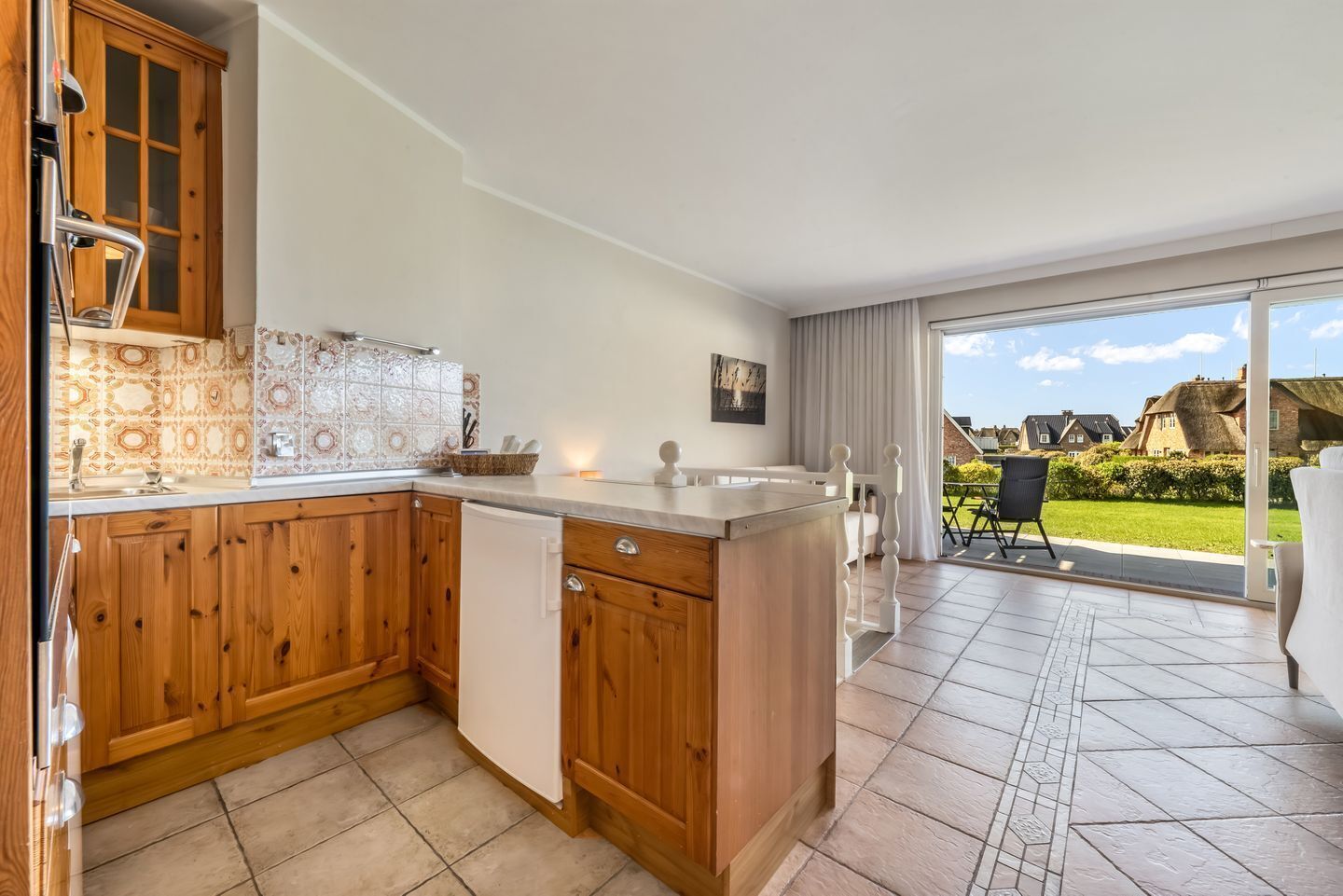 Una cocina con armarios de madera, un refrigerador blanco y una zona de comedor con mesa y sillas.
