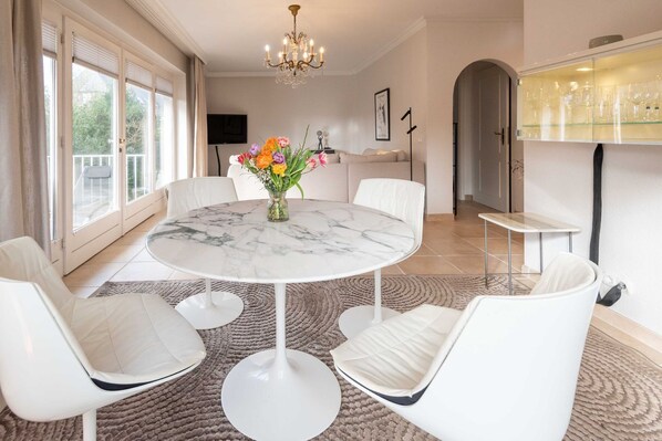 A modern dining room with a marble table, white chairs, and a vase of flowers. - Haus Gorch-fock-straße - Exklusives Hausteil mit ca. 120 m² und 5 Zimmern, für bis zu 4 Personen (Sylt)