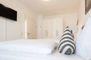 Quarto com duas camas, roupa de cama branca, almofada listrada e guarda-roupa com várias portas.