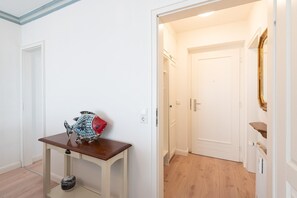 A hallway with a wooden table, a decorative fish sculpture, and a door leading to a room with a mirror and a shelf. - Schloss am Meer, App. 10 - 2-zimmer Ferienwohnung in Bester Lage mit ca. 48 m² Wohnfläche, für 2 (Wenningstedt-Braderup (Sylt))