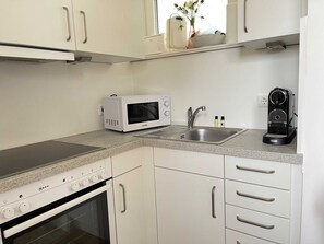 Cozinha moderna com armários brancos, micro-ondas embutido, máquina de café e pia de aço inoxidável.