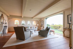 A spacious living room with a fireplace, a large window, and a view of the outdoors. - Haus Wattenblick - Reetgedecktes Einzelhaus auf ca. 280 m² Wohnfläche für bis zu 6 Personen mit (Wenningstedt-Braderup (Sylt))