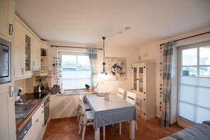 Cozinha compacta com armários brancos, uma mesa de jantar com cadeiras, uma janela com cortinas e uma obra de arte com tema de peixes na parede.