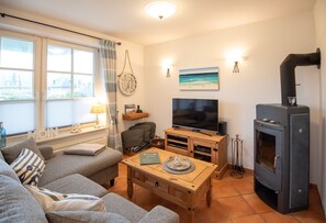 Uma sala de estar acolhedora, com sofá, televisão, mesa de centro de madeira e lareira a lenha.