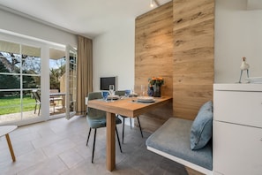 Een moderne eetruimte met een houten tafel, stoelen en uitzicht door grote glazen deuren op een tuin.