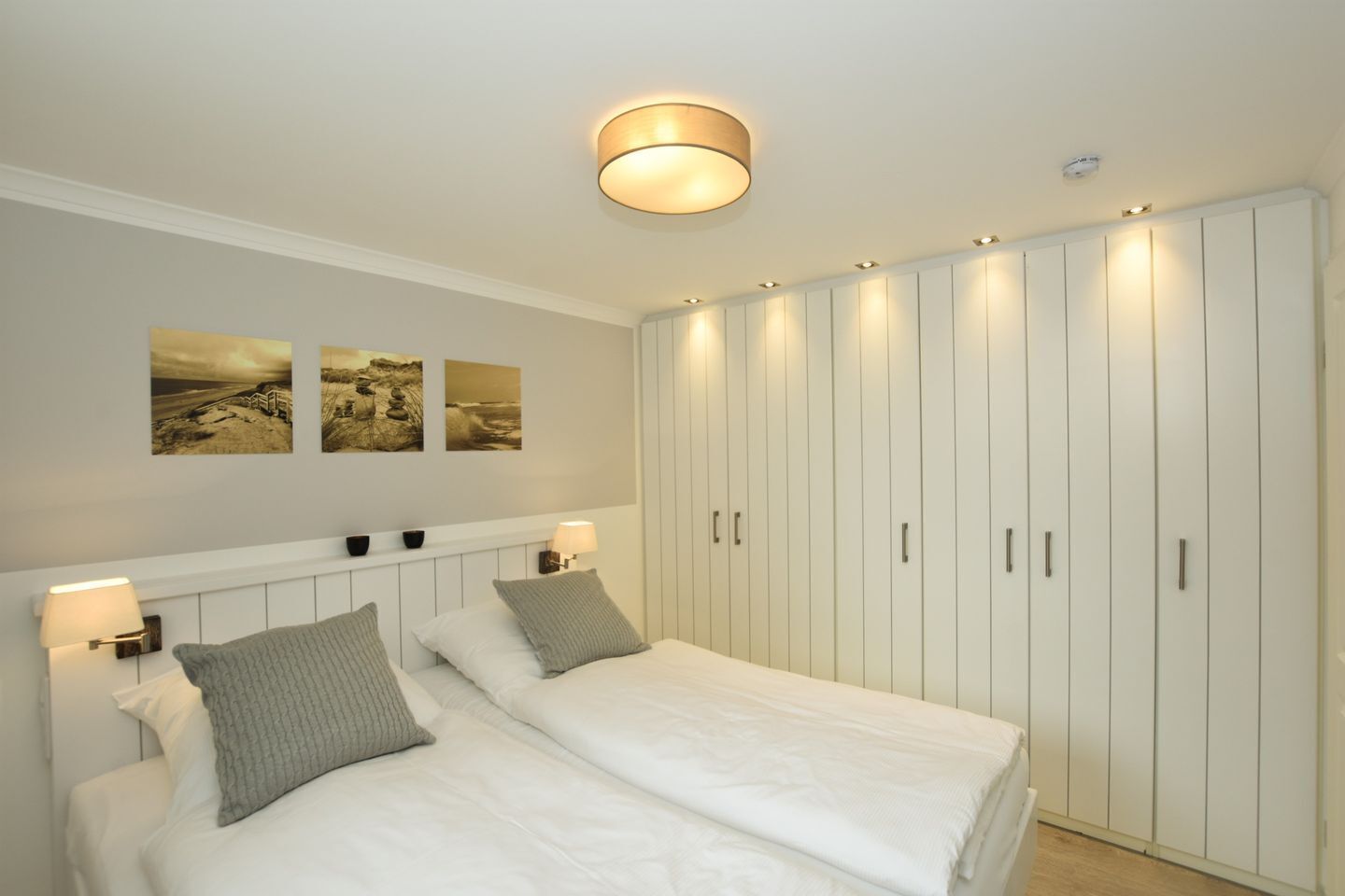 Een slaapkamer met twee bedden, een grote kledingkast, wandlampen en drie landschaptaferelen.