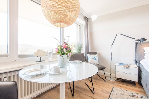 Une chambre d’hôtel moderne avec une table à manger ronde, une chaise blanche, une table de chevet avec une lampe et une vue sur l’extérieur.
