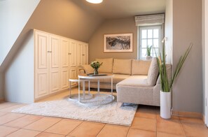 Un salon chaleureux avec un canapé, une petite table ronde, un meuble blanc et une grande fenêtre avec des rideaux.