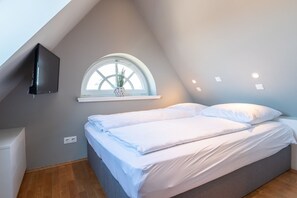 Une chambre à coucher avec un lit, une fenêtre agrémentée d’une plante et un téléviseur fixé au mur.