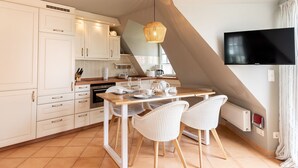 A modern kitchen with white cabinets, a wooden dining table, and wicker chairs. - LH Strandgeflüster, App.2 - Gemütliche 2-zimmer Ferienwohnung mit ca. 48 m² Wohnfläche, für 2 (Wenningstedt-Braderup (Sylt))