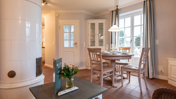 Un coin repas avec une table ronde, des chaises, un vase de fleurs et une télécommande posée sur la table.
