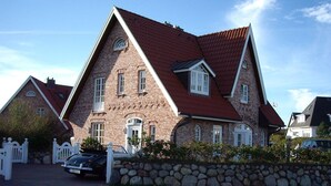 Une grande maison à deux étages, construite en briques, avec un toit à forte pente et de nombreuses fenêtres.