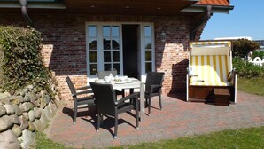 Une maison en briques avec un toit en tuiles, un mur en pierre et une terrasse dallée.